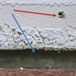 Kuva 1. Tyypillinen tapaus, jossa on tehty tiivistys. Lattian ja seinän rajakohta (sininen nuoli) on massatiivistetty, mutta jalkalistan naulanreikä on jäänyt tiivistämättä (punainen nuoli).