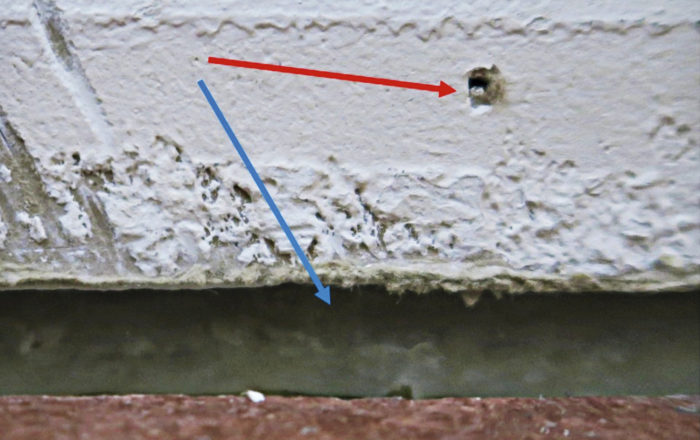 Kuva 1. Tyypillinen tapaus, jossa on tehty tiivistys. Lattian ja seinän rajakohta (sininen nuoli) on massatiivistetty, mutta jalkalistan naulanreikä on jäänyt tiivistämättä (punainen nuoli).